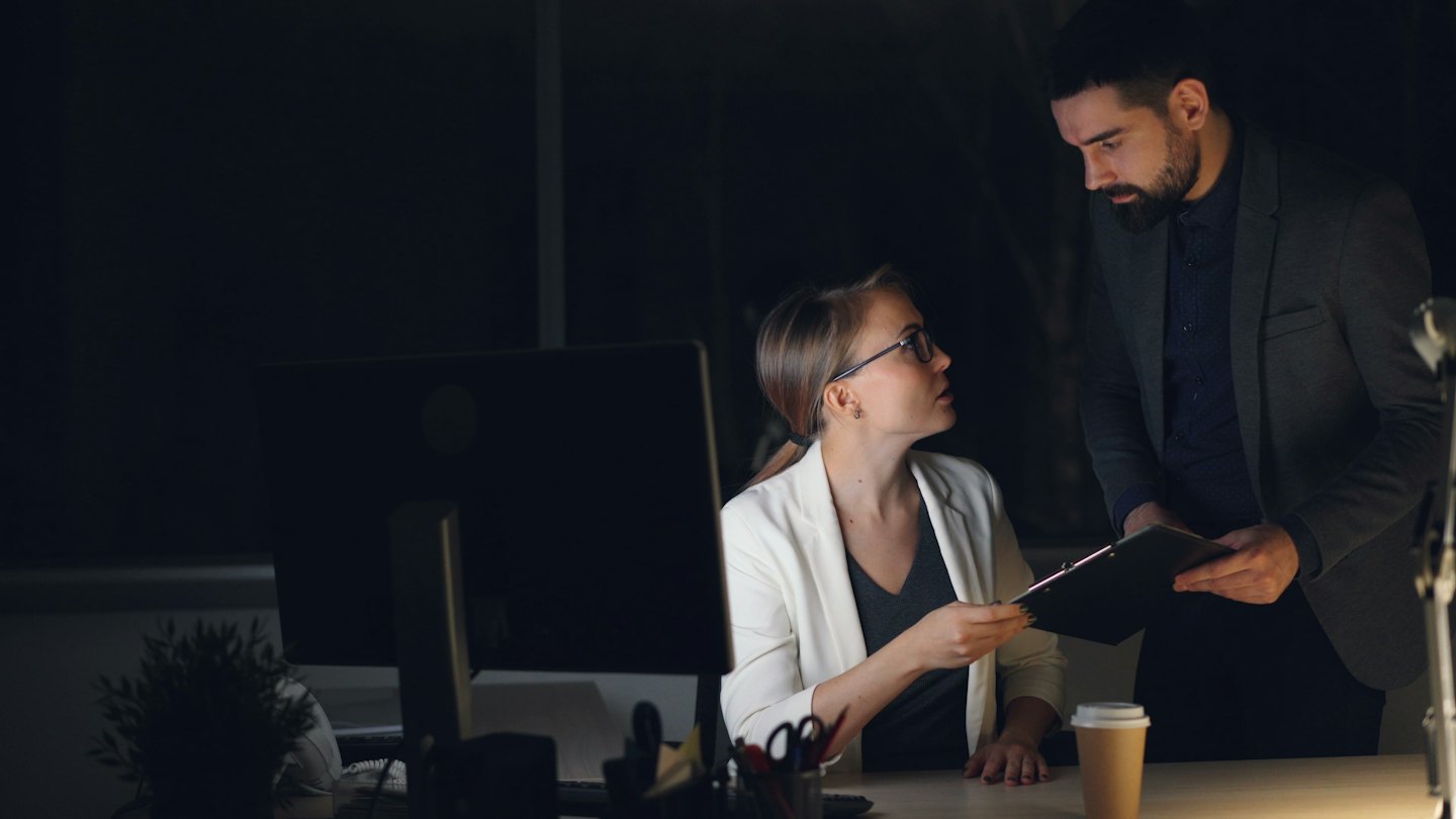 Professionisti aziendali che discutono documenti a una scrivania a tarda notte.