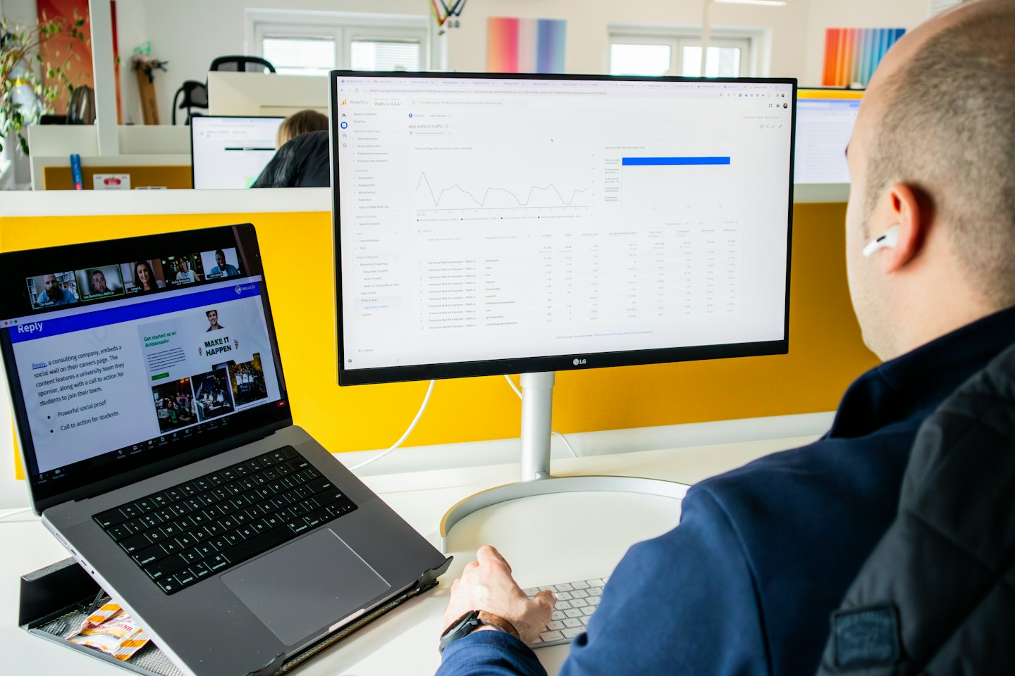 Uomo con auricolare digita su tastiera alla scrivania d'ufficio con monitor di analisi.